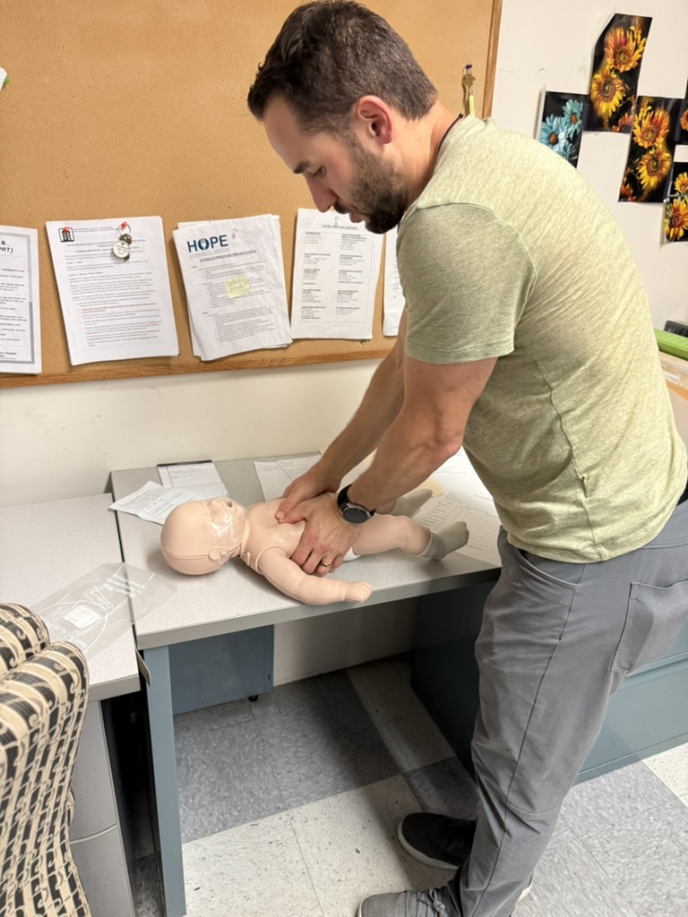 Instructor demonstrating infant CPR on a training manikin at a desk